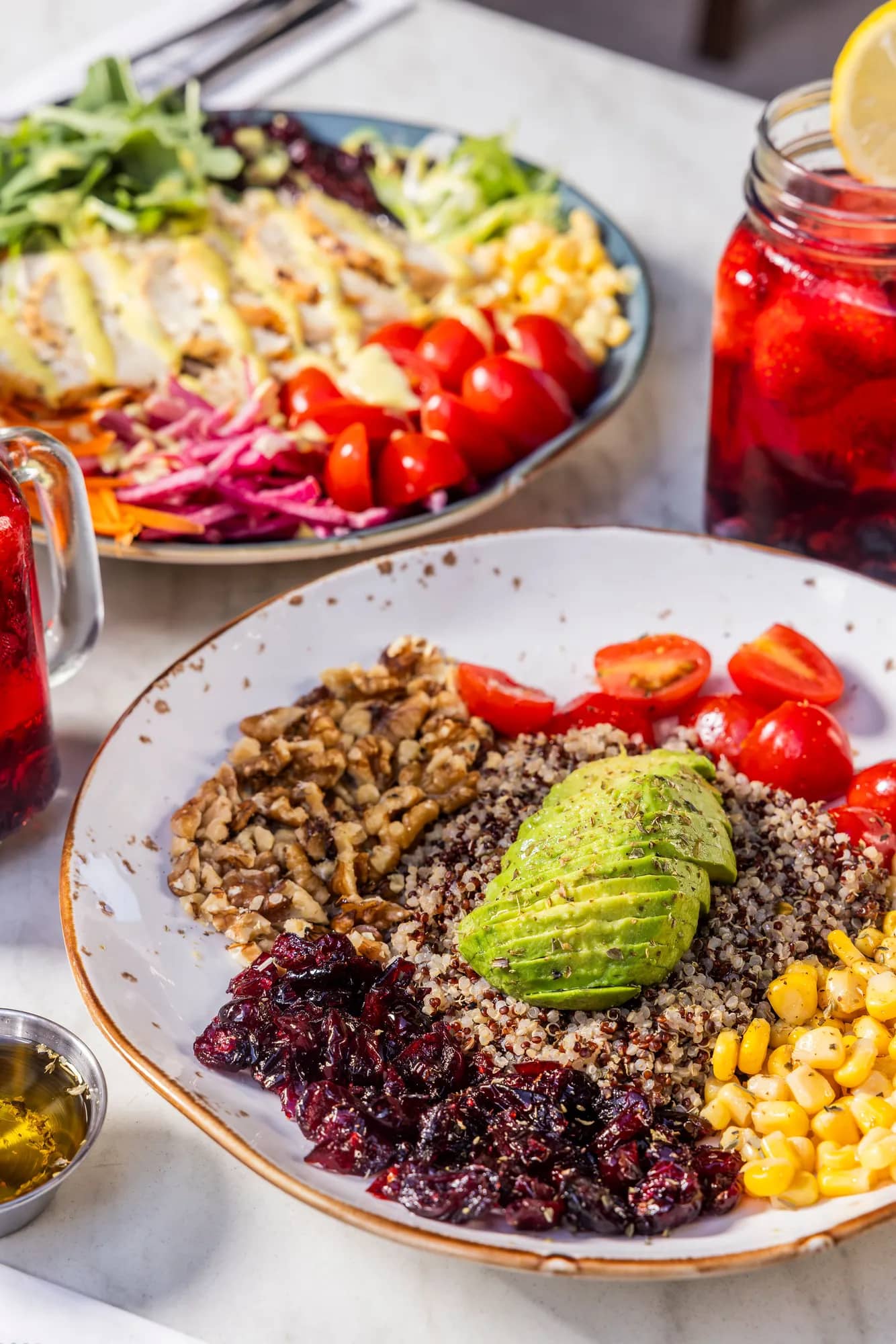 Quinoa salad bowl with avocado, walnuts, corn and cranberries beside a chicken salad and fruit iced tea