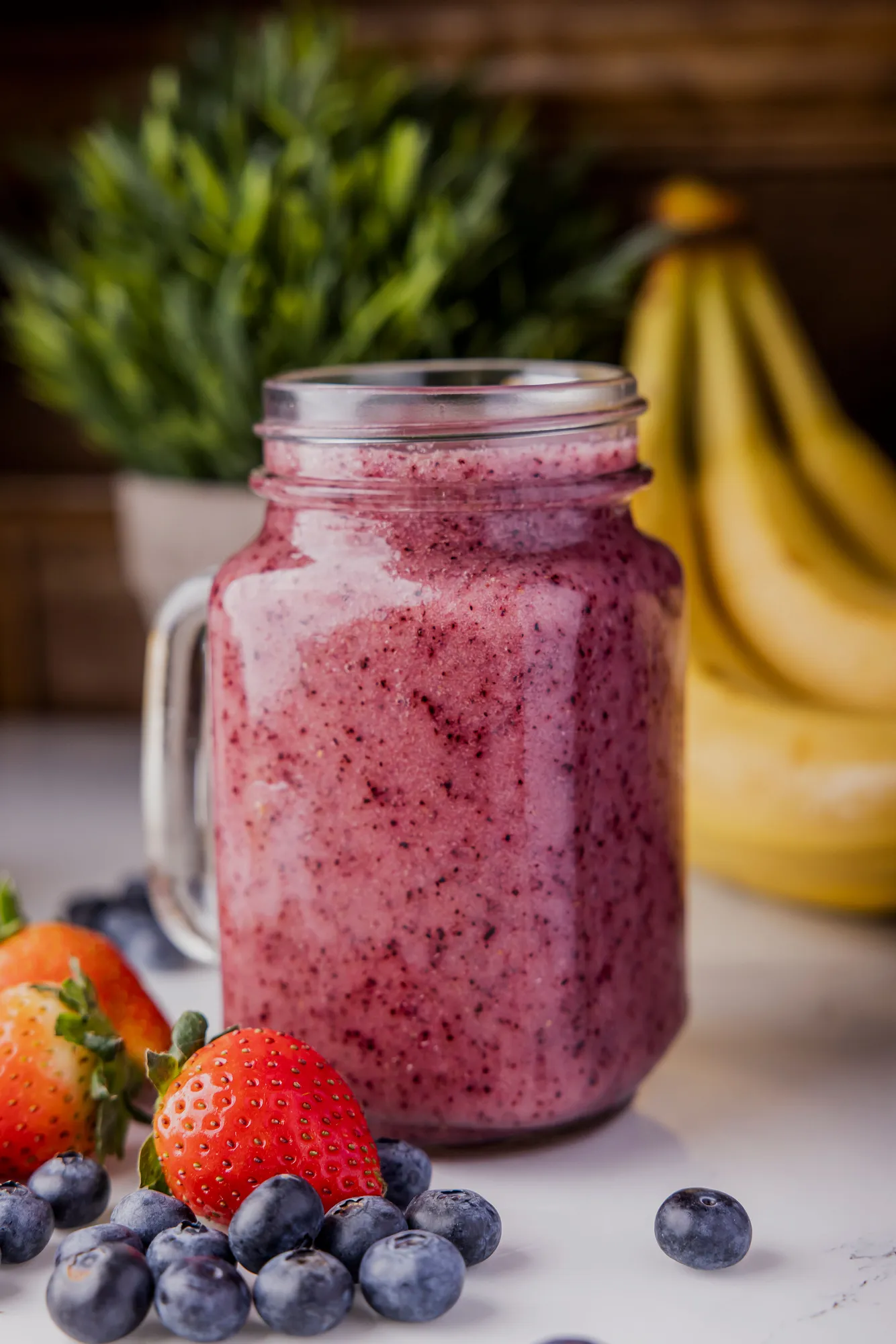 Berry smoothie in a mason jar with strawberries, blueberries and bananas in the background