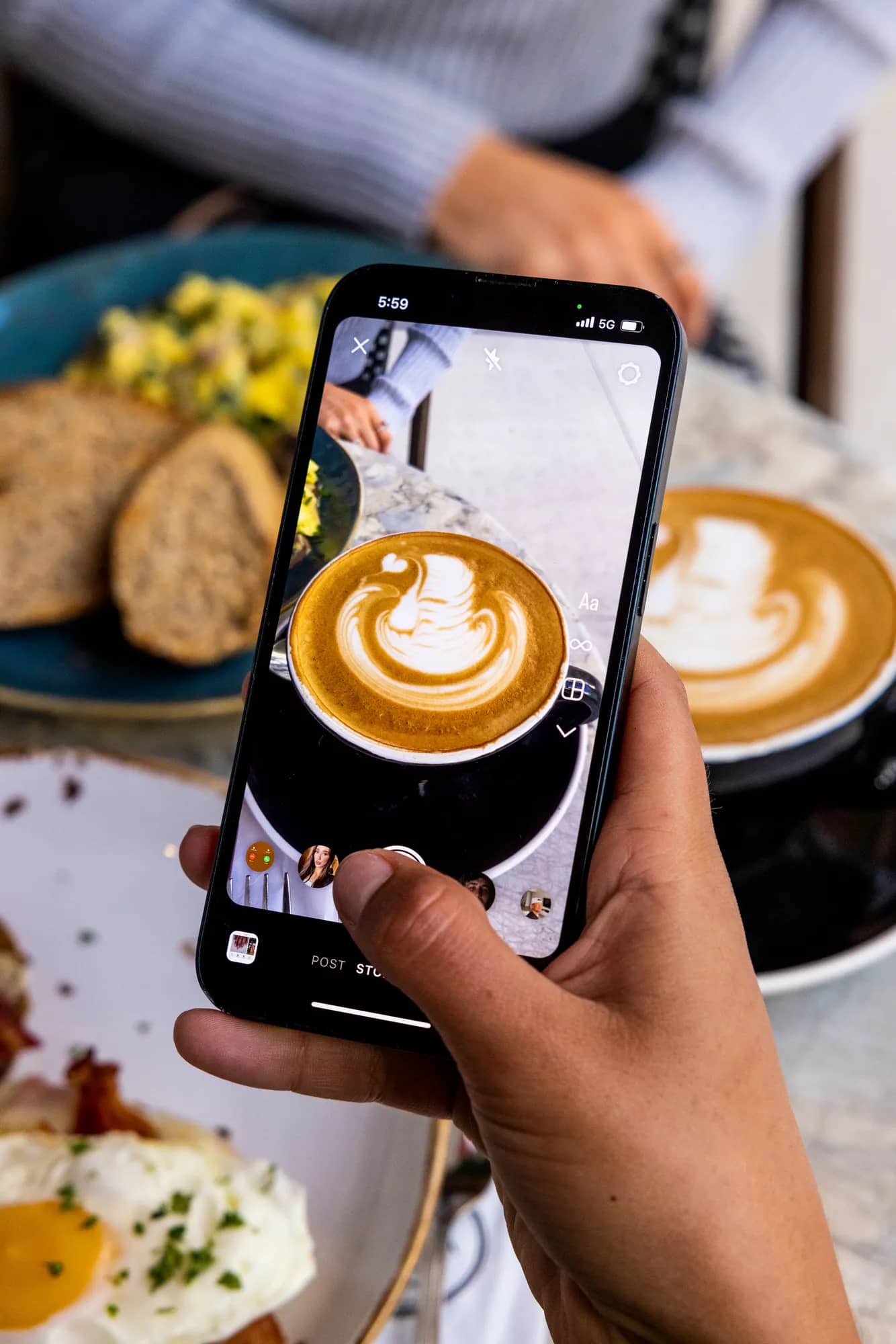Hand photographing a latte with heart-shaped foam art on a smartphone at a café table