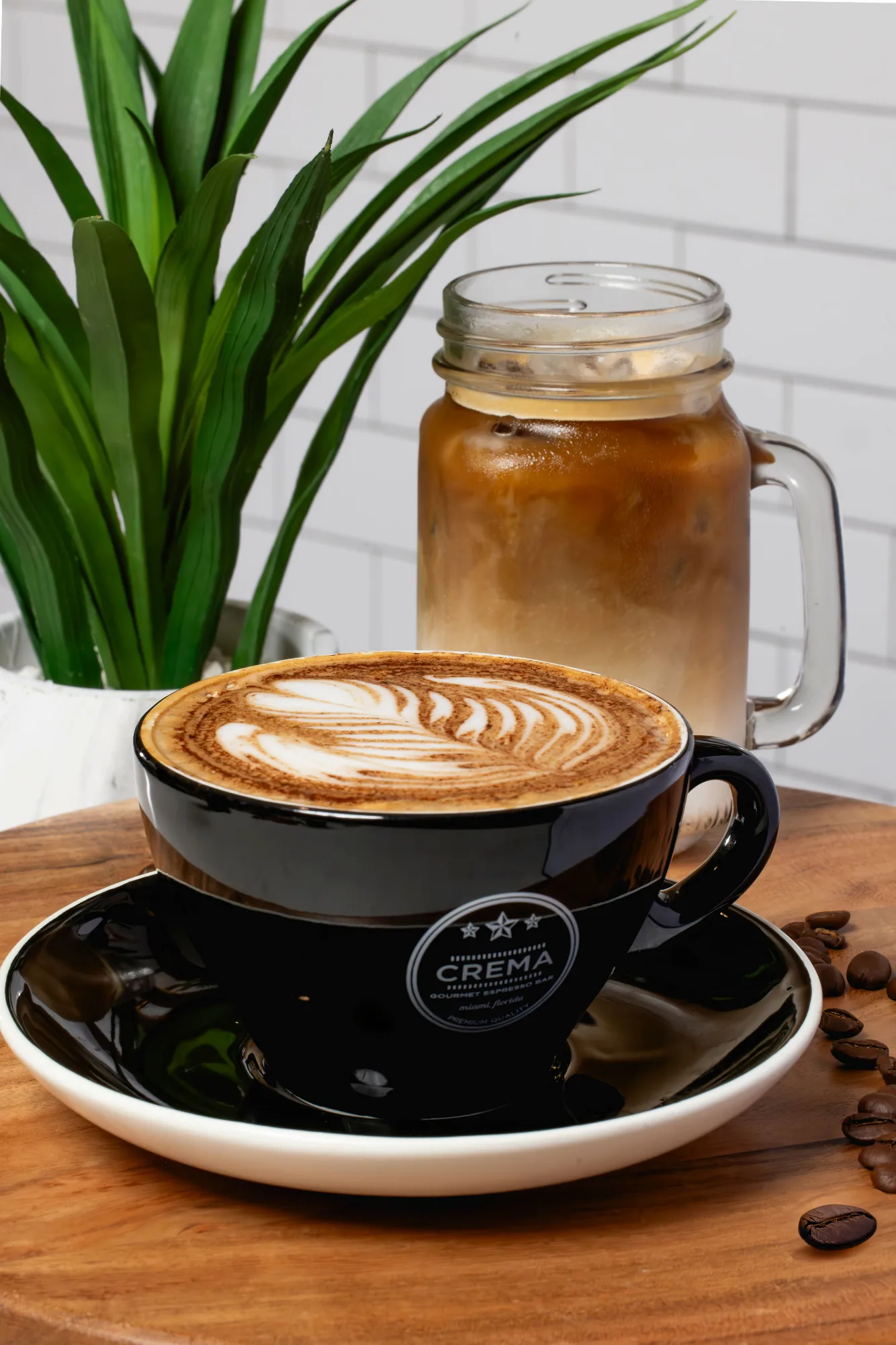 Latte with leaf-pattern latte art beside an iced coffee in a mason jar mug